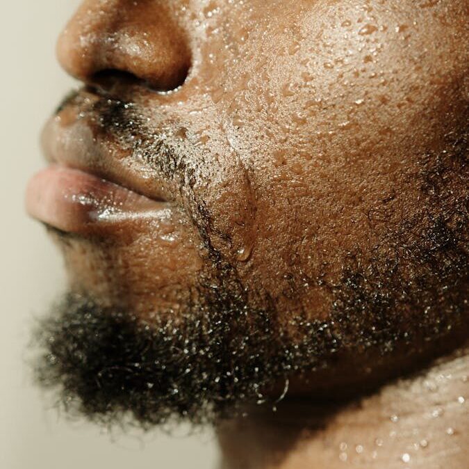 Intimate close-up of a bearded man with water droplets on his face, conveying a fresh and vibrant feeling.
